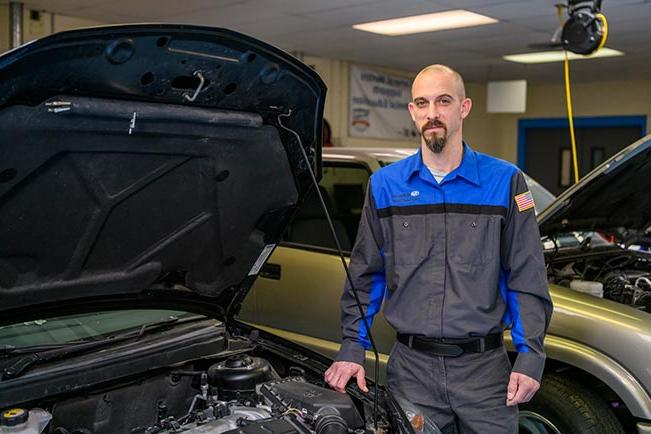 Seth DeGraff standing with hood of car open in automotive lab